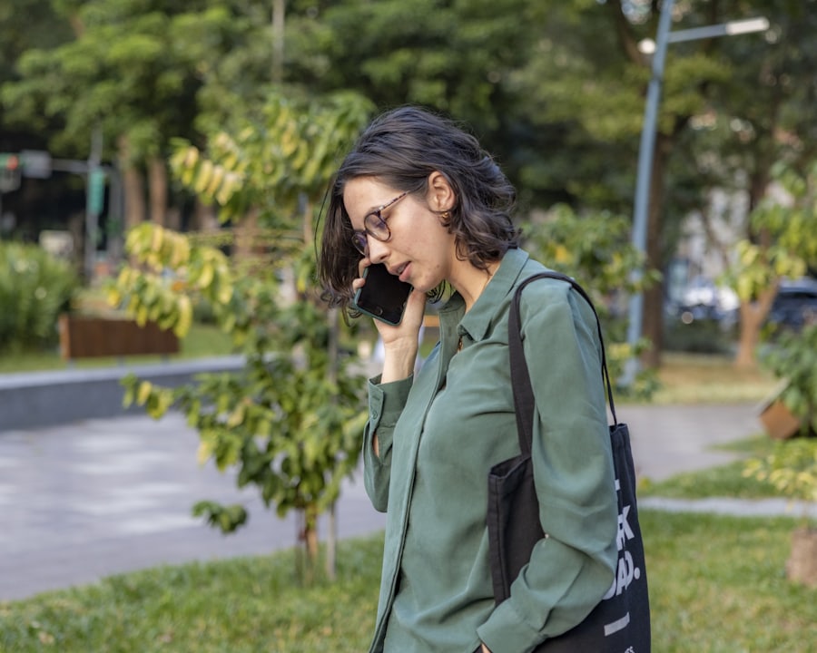 A person standing outdoors in a park, holding a phone to their ear
            mid-conversation.